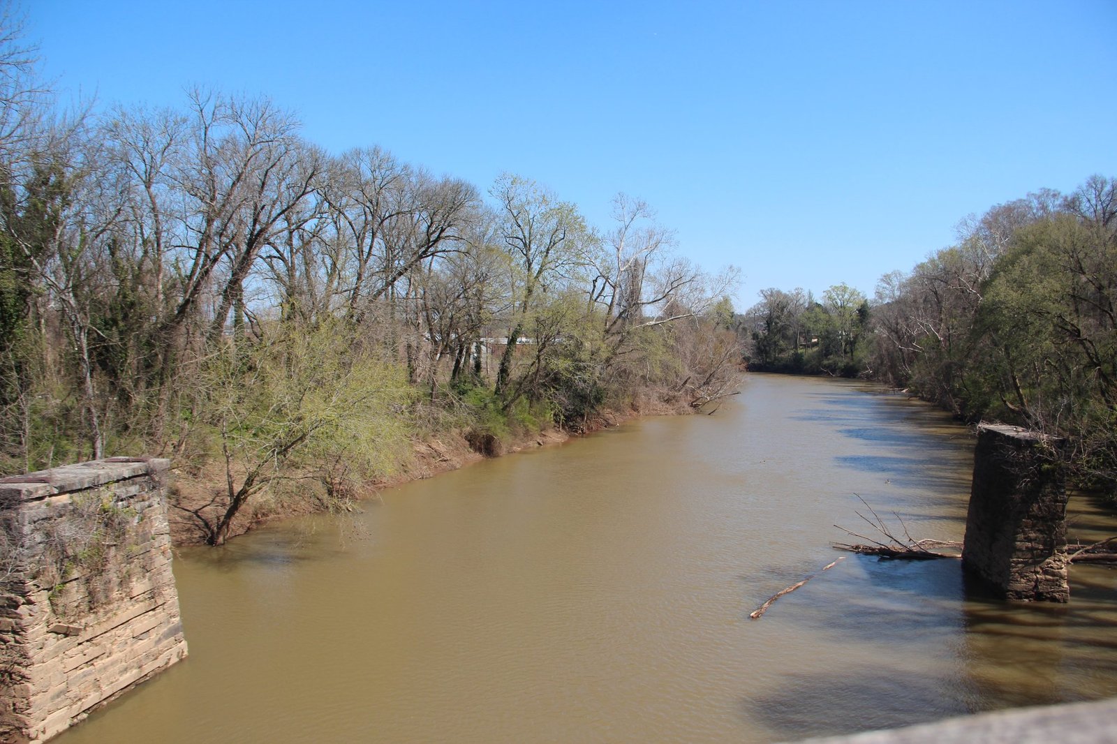 The Etowah River flowing between wooded banks and old bridge piers in Rome, Georgia