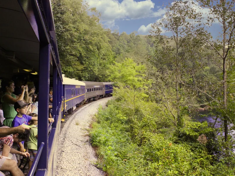 Riders leaning out of open-air cars on the Blue Ridge Scenic Railway along the Toccoa River