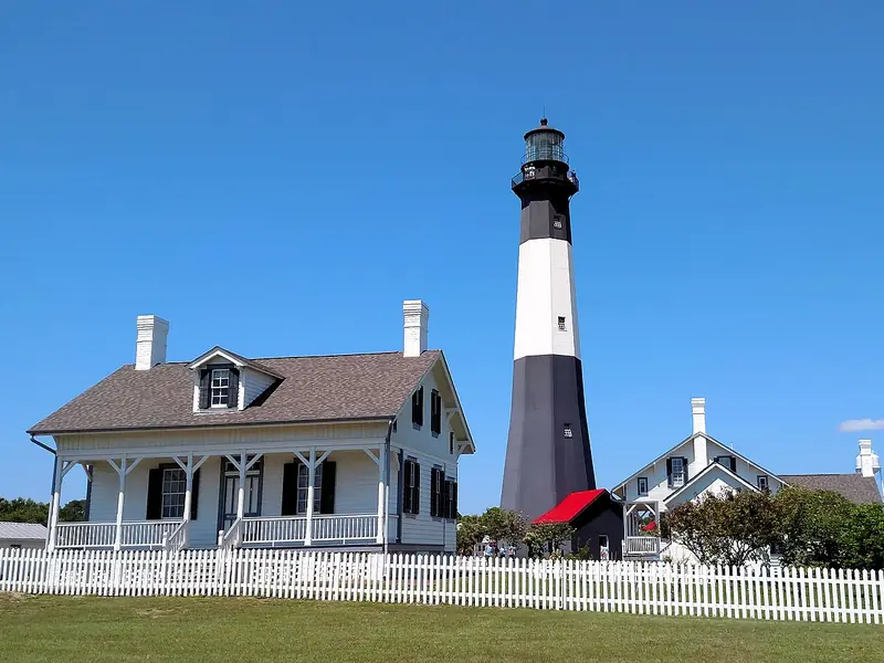 Black-and-white Tybee Island Lighthouse beside the white lightkeeper&rsquo;s house