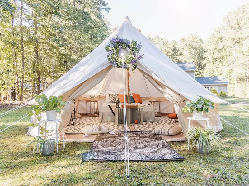 A furnished bell tent with rugs, cushions and string lights under pine trees