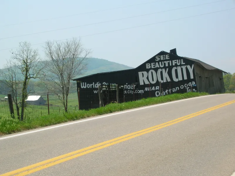 A black barn painted with See Beautiful Rock City beside a rural highway