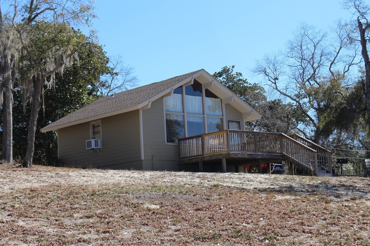A cottage with a wall of windows and a wooden deck under live oaks at Little Ocmulgee State Park