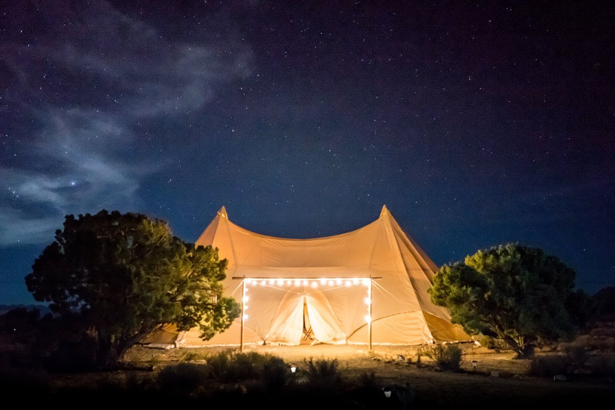A canvas glamping tent glowing with lights under a starry night sky