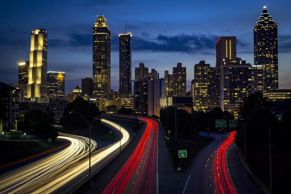 Downtown Atlanta skyline lit up at night above the light trails of Freedom Parkway, seen from the Jackson Street Bridge